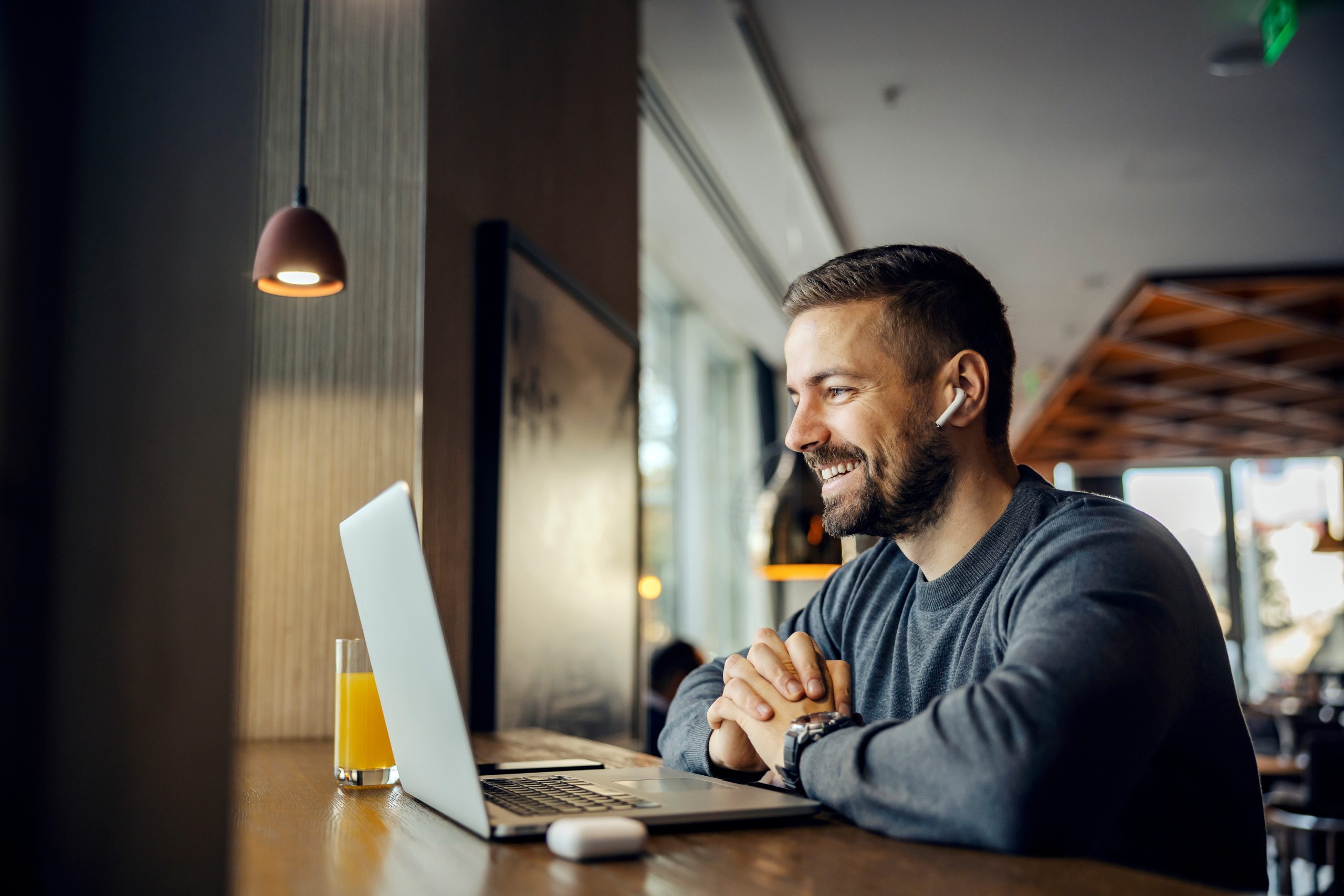 A happy remote worker is sitting in cafeteria and having online meeting with clients.