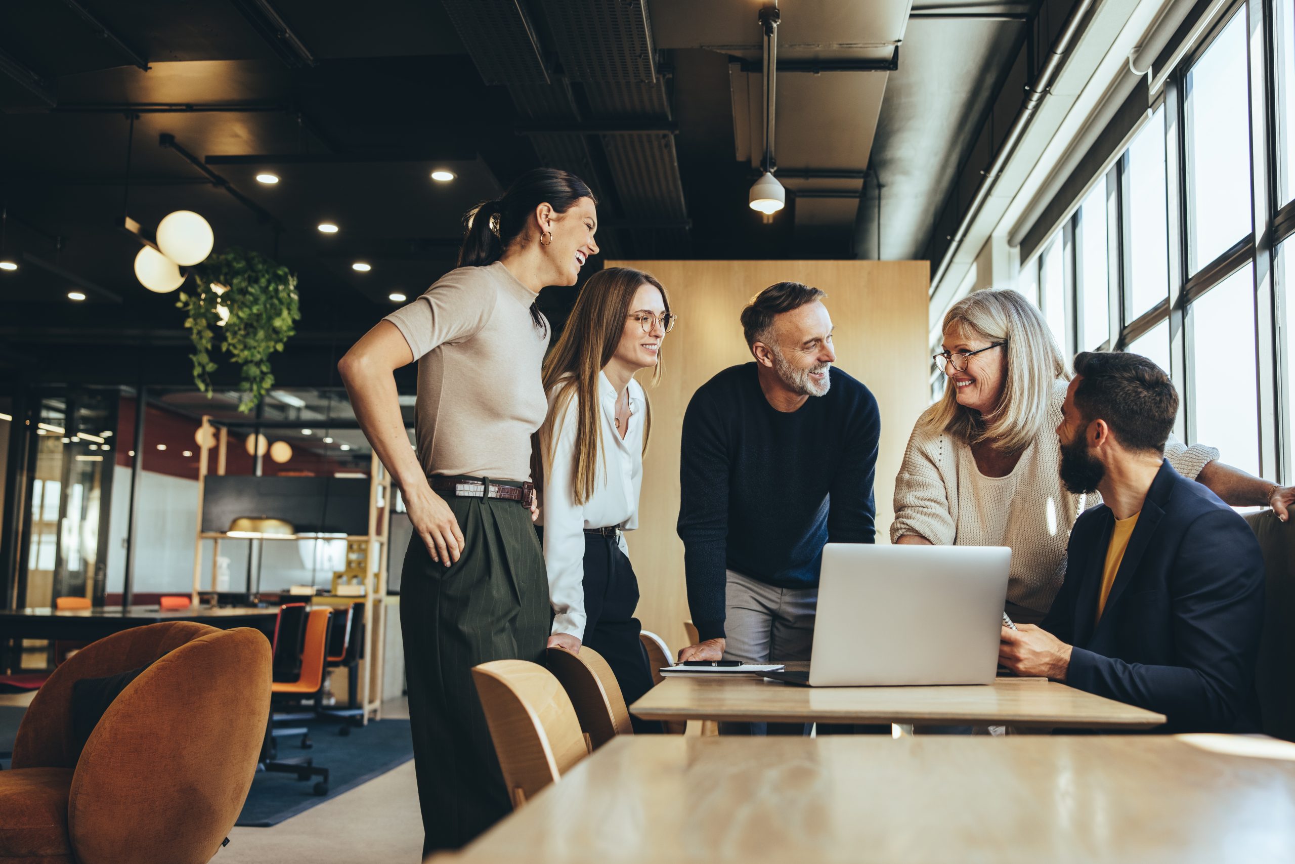 Smiling businesspeople having a discussion in an office Smiling businesspeople having a discussion while collaborating on a new project in an office. Group of happy businesspeople using a laptop while working together in a modern workspace.
