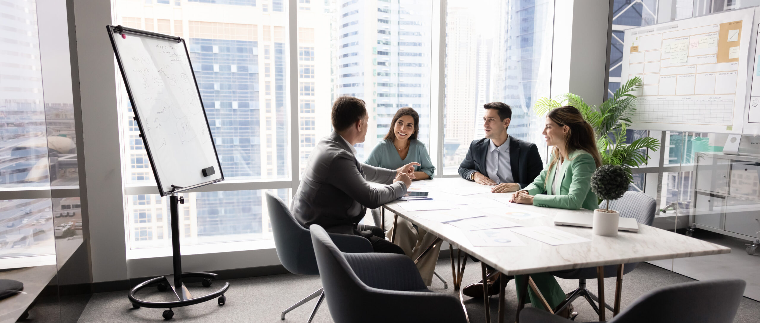 Diverse corporate team holding discussion by conference table in boardroom Diverse corporate team holding open discussion by conference table collaborating on shared project exchanging ideas insights on strategic development interacting on staff briefing in modern boardroom